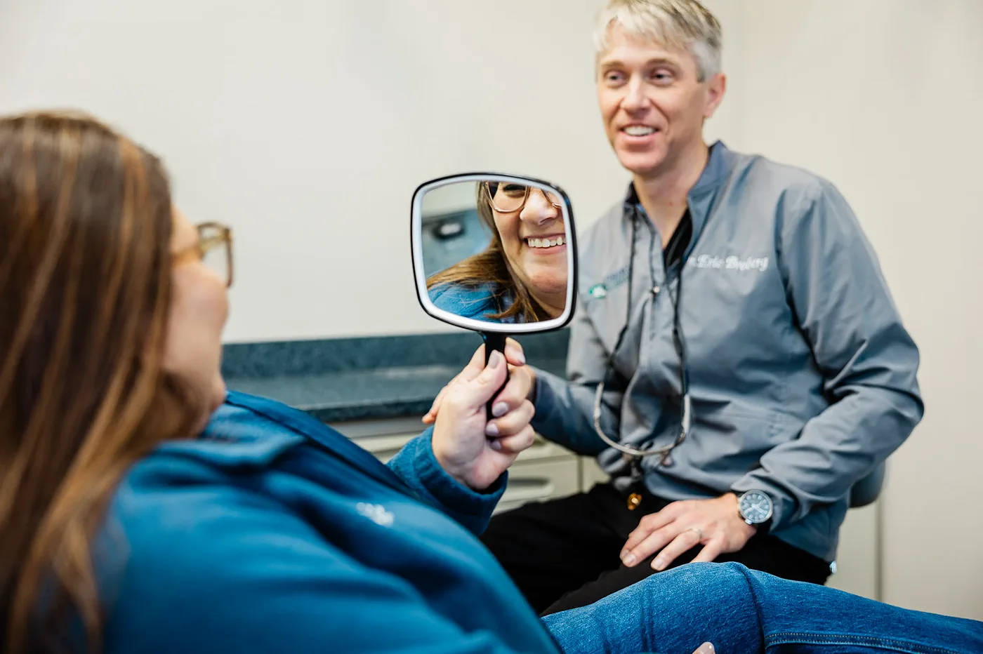Patient reviewing her smile in a mirror during a dental veneers consultation with Dr. Broberg